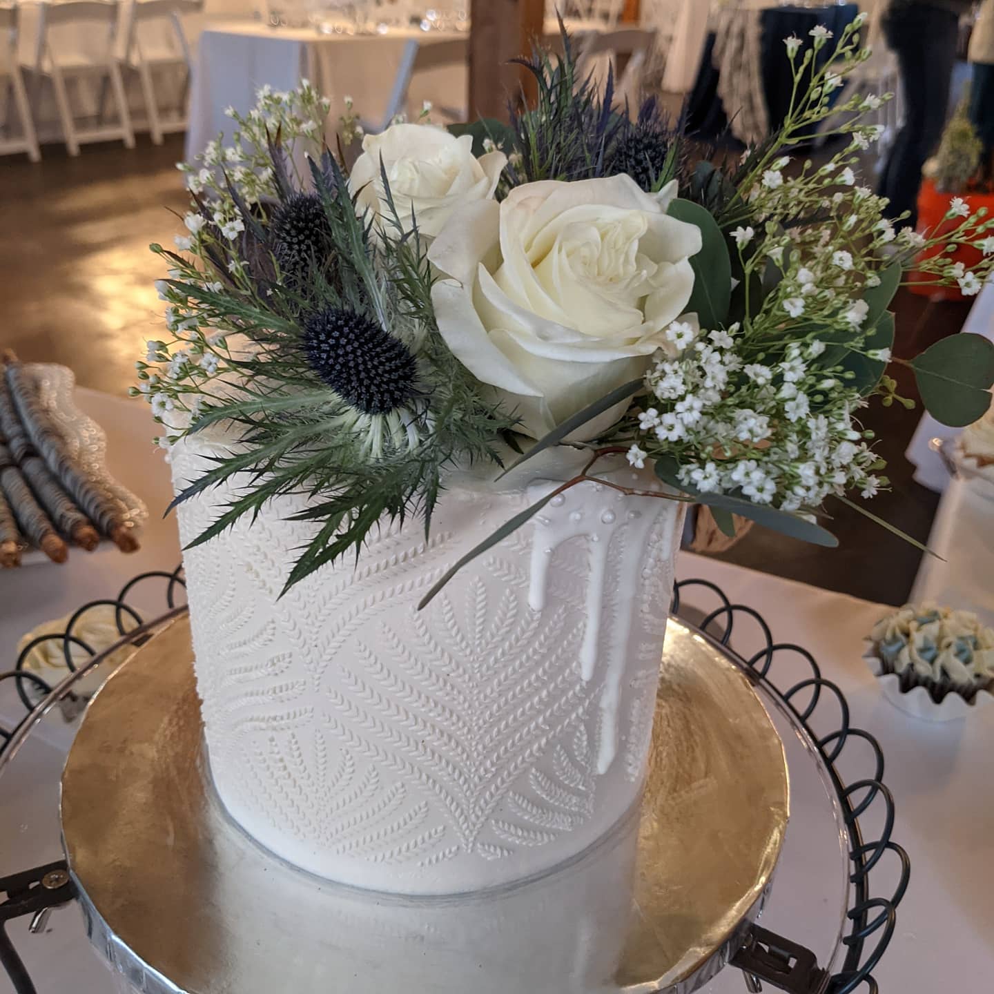 White textured buttercream cake topped with roses, thistle and eucalyptus