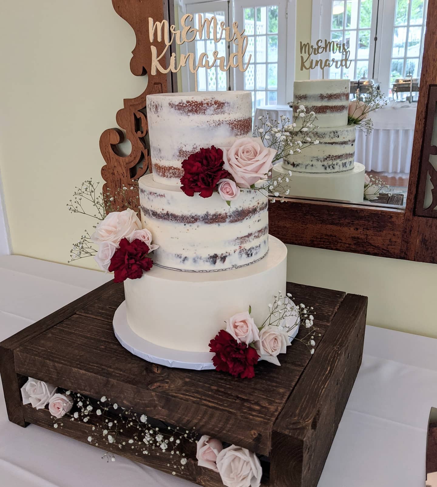 Three-tier semi-naked wedding cake with burgundy and blush flowers