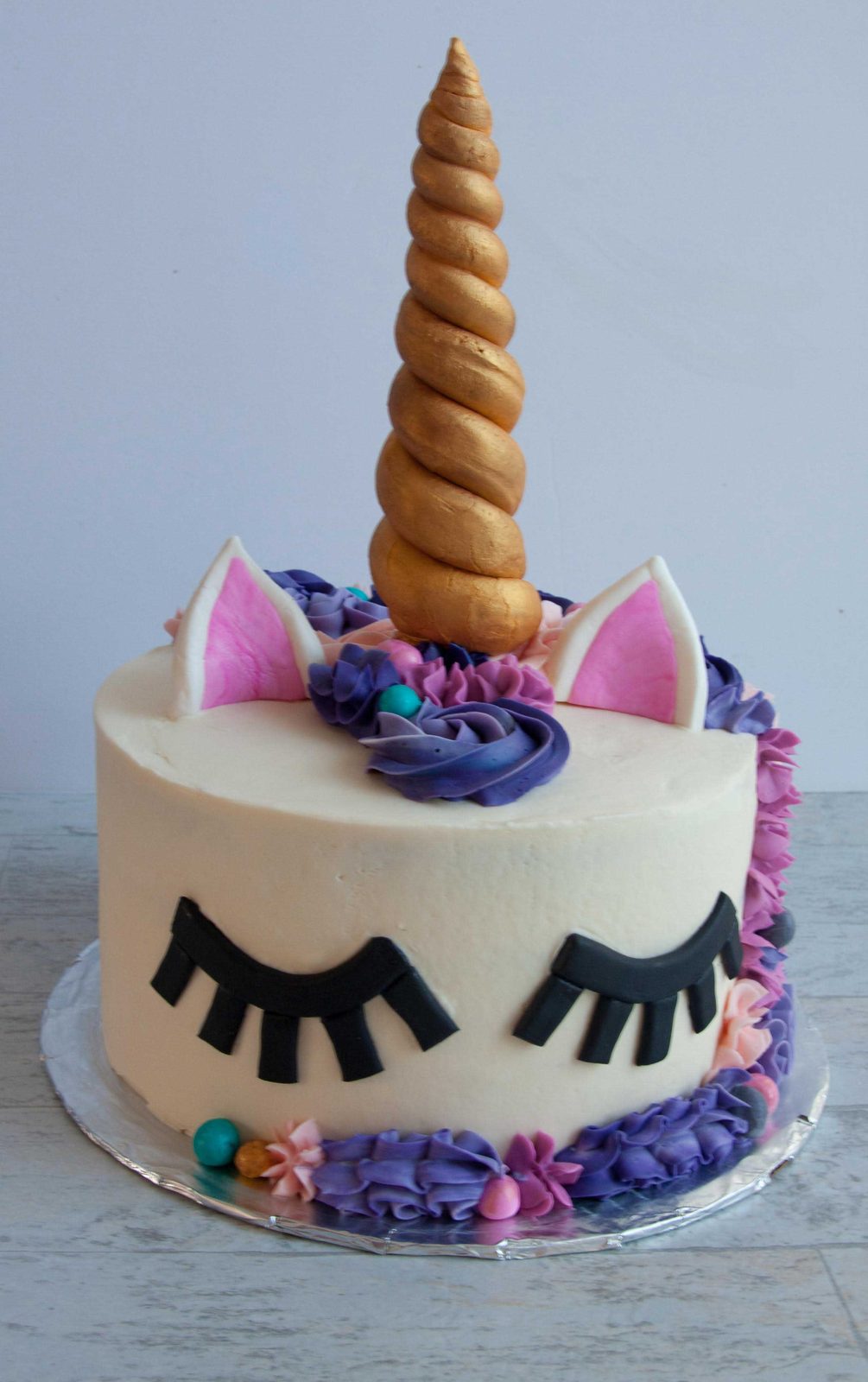 Unicorn cake with a gold horn, closed eyes and a buttercream flower mane
